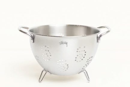 A stainless steel Stüssy strainer with an etched logo next to a branded glass pour over coffee server.