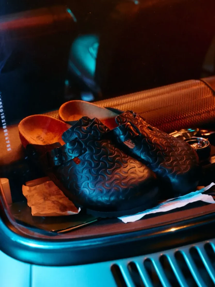 A sleek smooth black leather clog featuring a deeply embossed bone pattern across the entire upper.