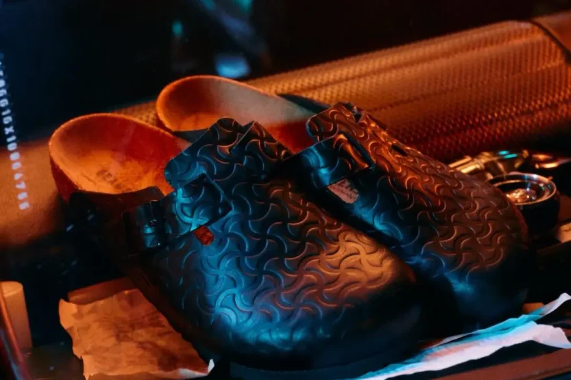 A sleek smooth black leather clog featuring a deeply embossed bone pattern across the entire upper.