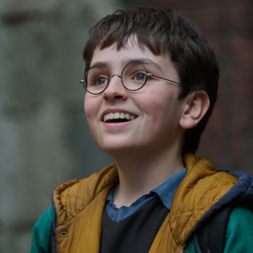 The new Harry Potter in HBO Max's new Harry Potter Series. Harry Potter is wearing a green jacket with yellow accents and he's slightly looking up with a smile.